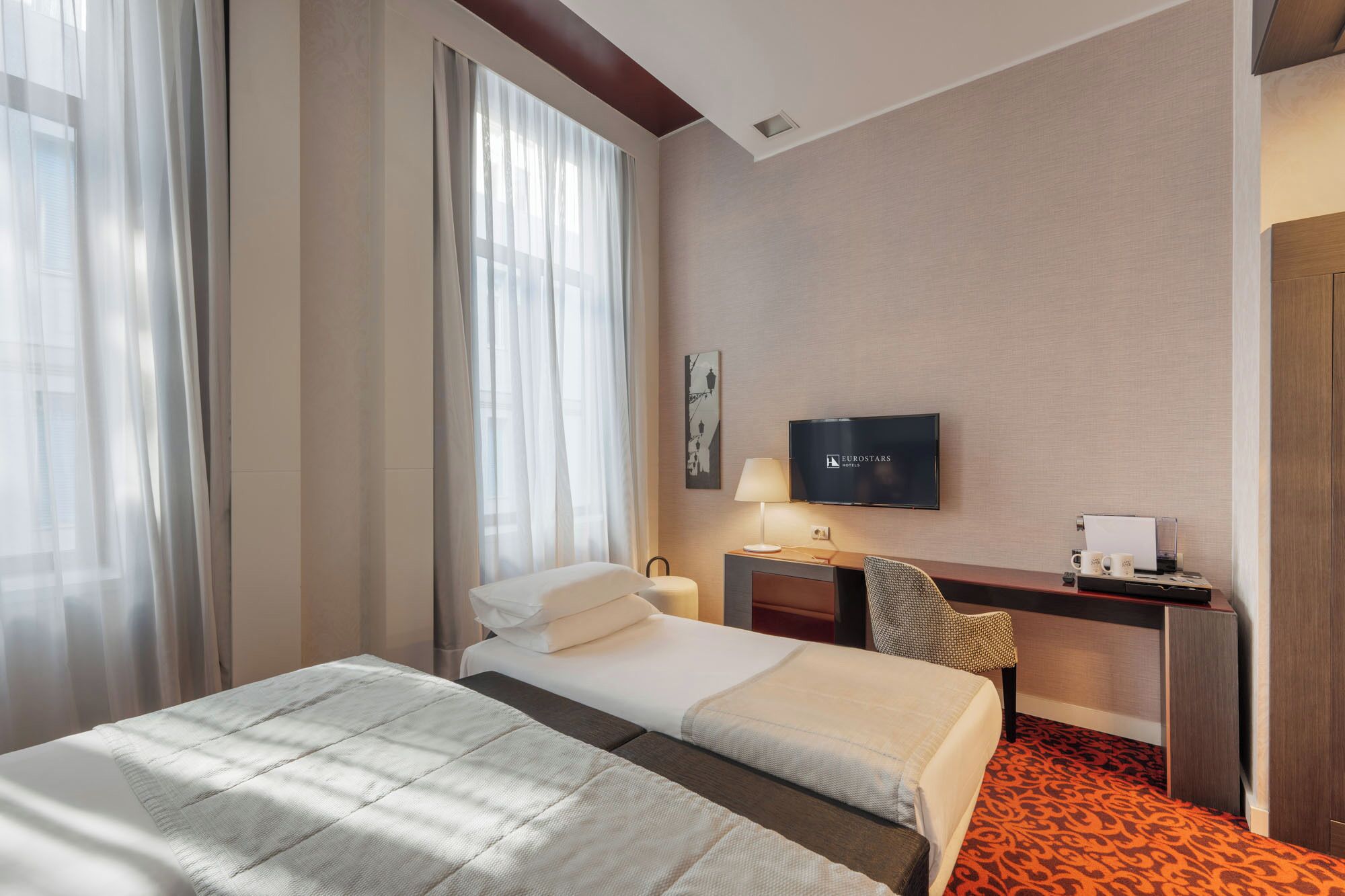 A hotel room with a bed, a desk, a TV, and a window with curtains.