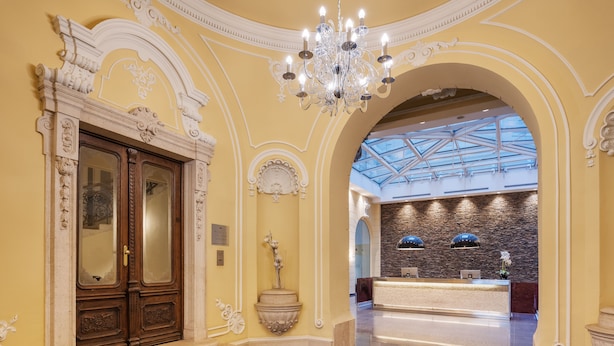 Un vaste hall d’entrée agrémenté de boiseries ouvragées, d’un lustre, d’un comptoir de réception et d’une verrière.