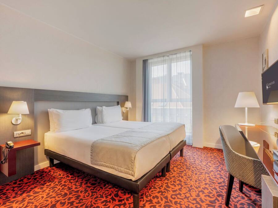 Habitación de hotel con una cama grande, lámparas de noche, un escritorio con silla y un televisor en la pared.