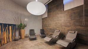 Un espace d’attente comprenant deux fauteuils confortables, une grande plante en pot et un téléviseur fixé au mur.