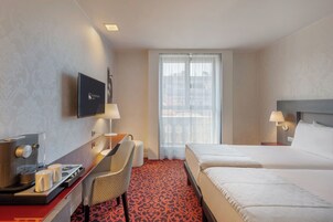 Une chambre d’hôtel comprenant un lit, un bureau avec une machine à café, une chaise, un téléviseur et une grande fenêtre avec des rideaux.
