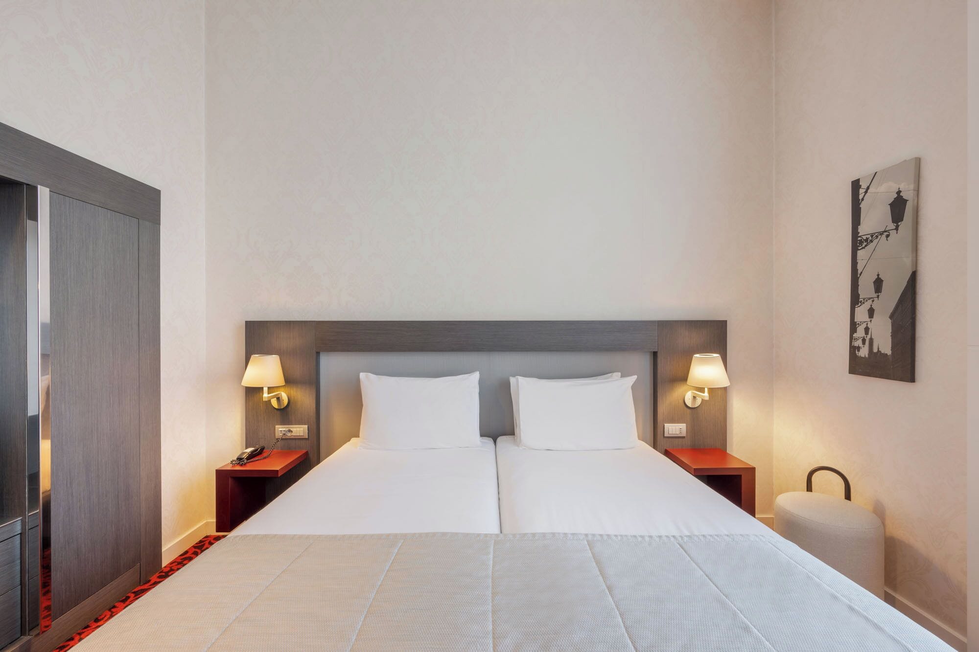 Habitación de hotel con una cama grande, dos mesitas de noche con lámparas, un atril y una lámpara de pared.
