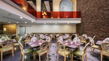 A spacious dining area with multiple tables and chairs, a high ceiling, and a stone wall.