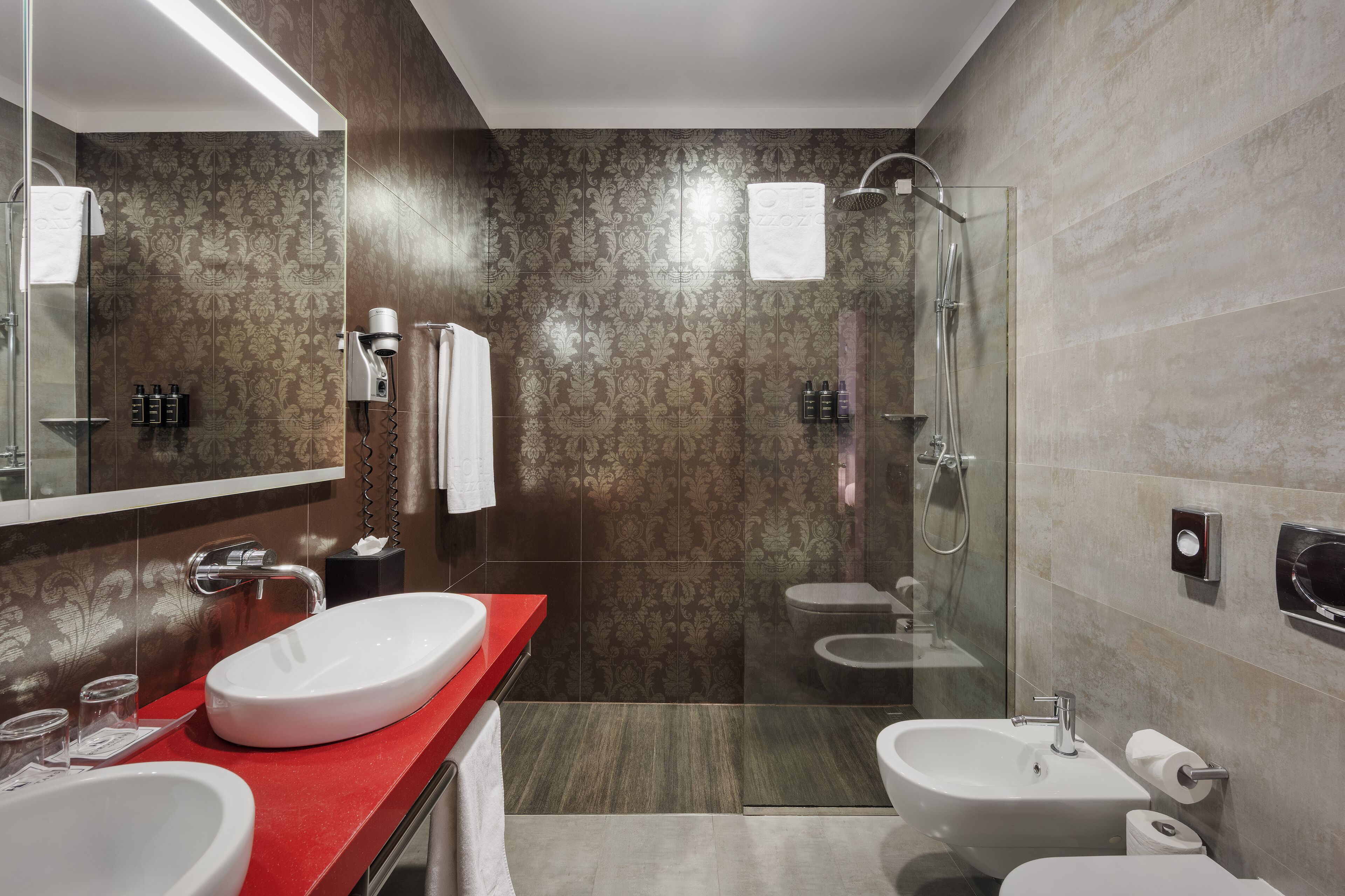 A modern bathroom with a large mirror, two sinks, a shower, and a toilet.