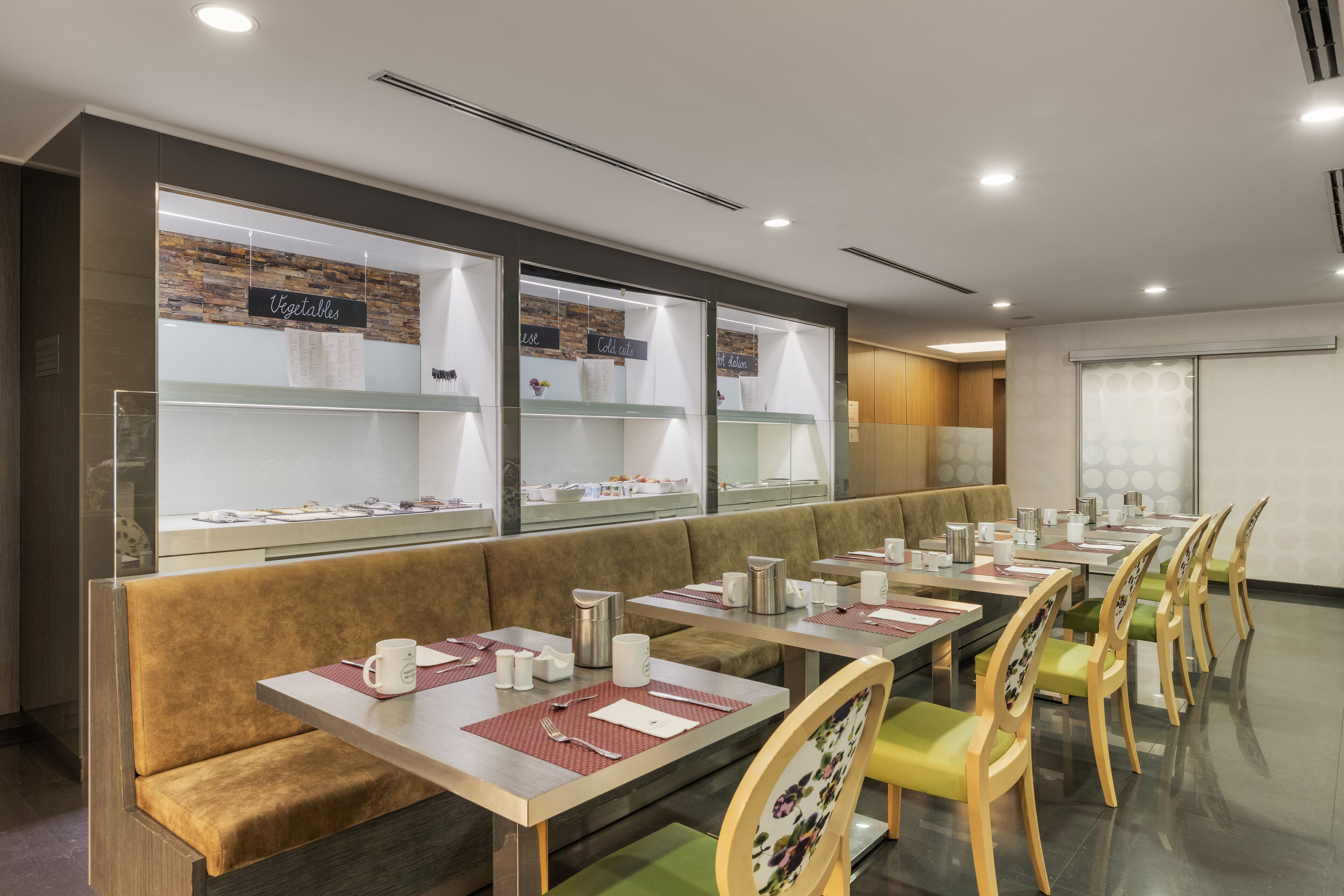 Un restaurante con varias mesas y cabinas, cada una con un panel de menú que muestra 'Verduras' y 'Embutidos'.