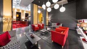 Un hall d’entrée moderne avec des canapés rouges, un canapé à motifs et une table basse. On y trouve des lampes sphériques suspendues et un lampadaire.