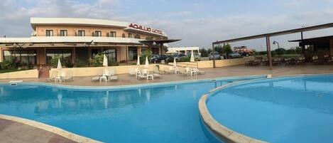 Una piscina al aire libre, sombrillas, sillones reclinables de piscina