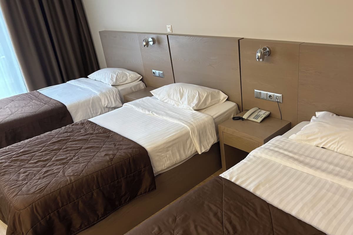 Habitación de hotel con tres camas, cada una con diferente ropa de cama. Se observa una mesita de noche con un teléfono y un enchufe.
