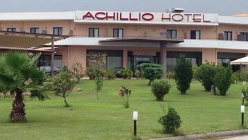 The exterior of the Achillio Hotel with a well-maintained lawn and a few small trees.