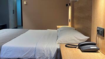 Una habitación de hotel con una cama, teléfono en la mesita de noche y cabecero de madera.