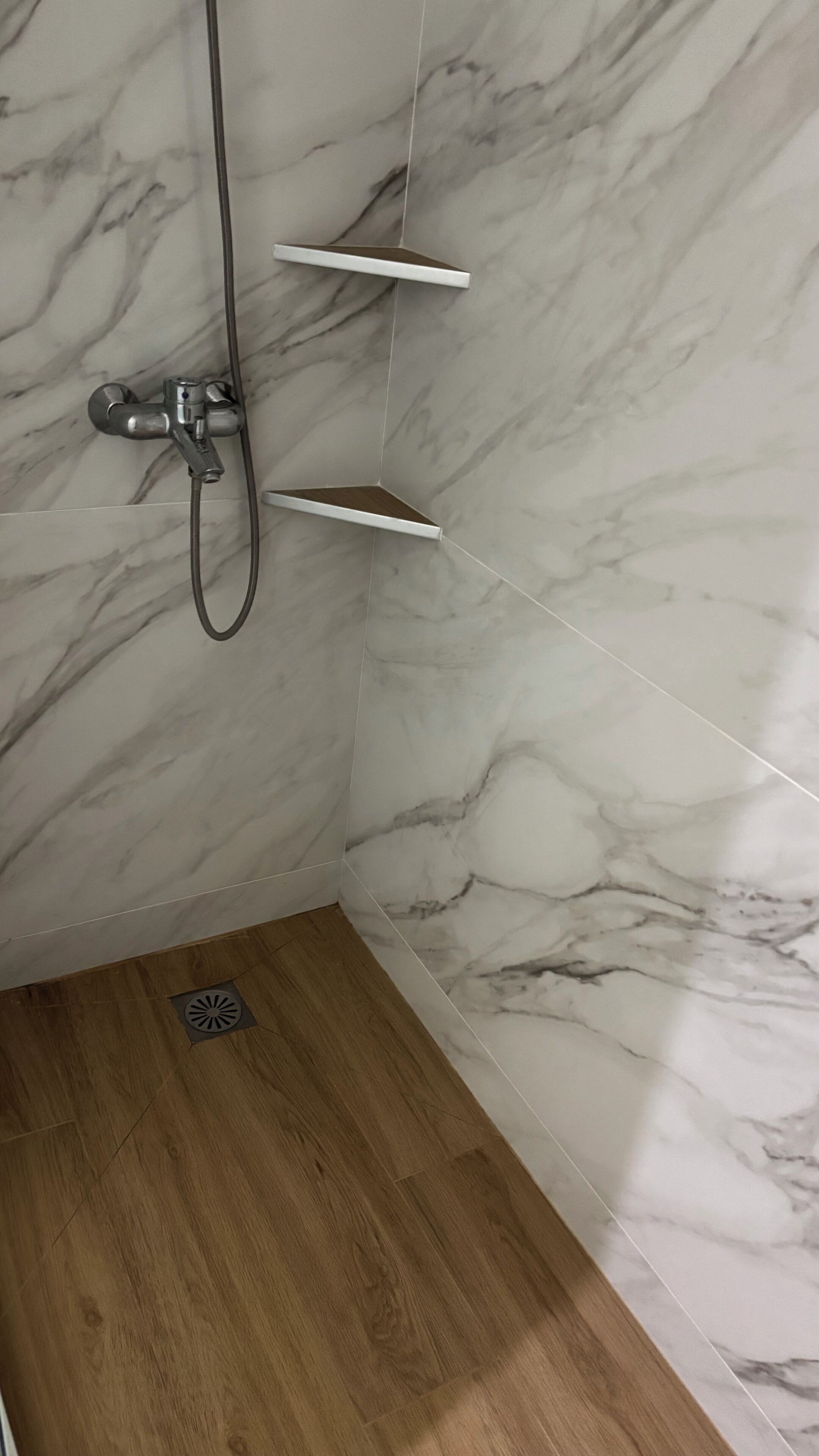A shower area with a marble wall, a wooden floor, and a metal showerhead.
