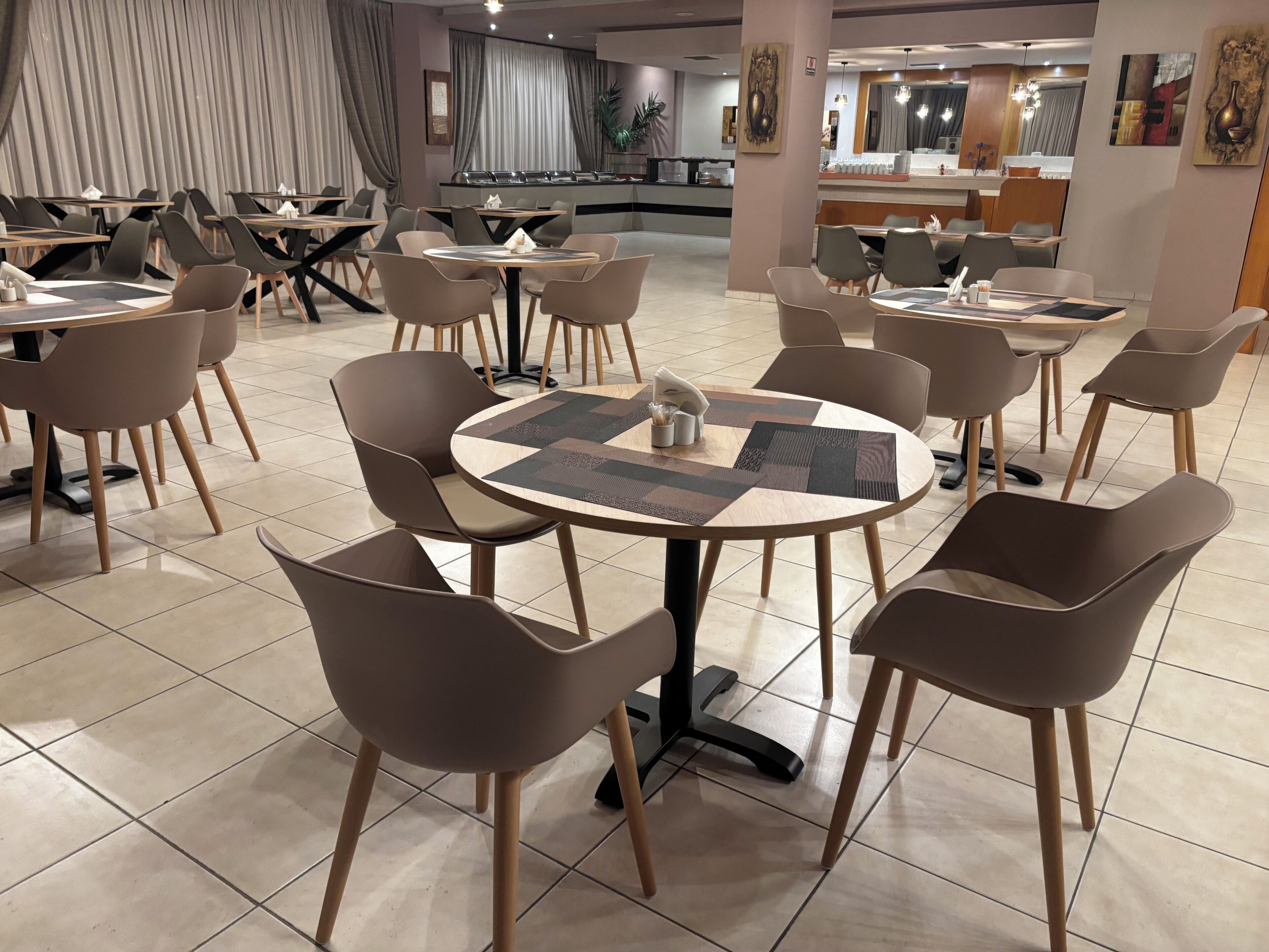 Een moderne eetruimte met ronde tafels en stoelen, een balie met een menukaart, en een groot raam met gordijnen.