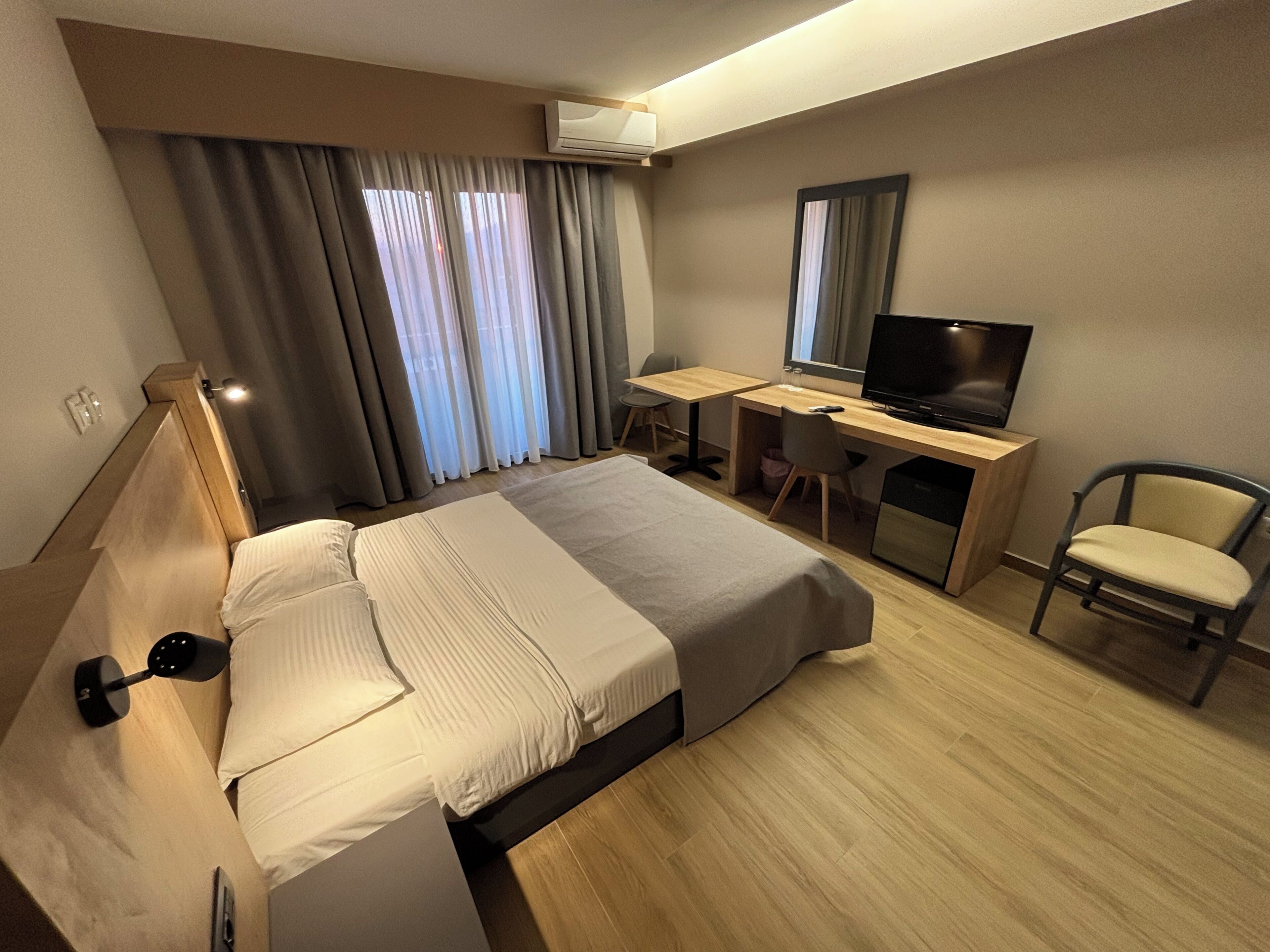 A hotel room with a bed, desk, chair, TV, and curtains.