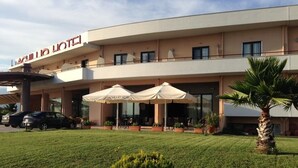 A hotel with a flat facade, outdoor seating area with umbrellas, and a well-maintained lawn. - Achillio Hotel (Komotini)