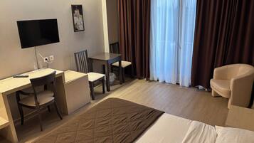 A hotel room with a bed, a desk, two chairs, a television, and a window with curtains.
