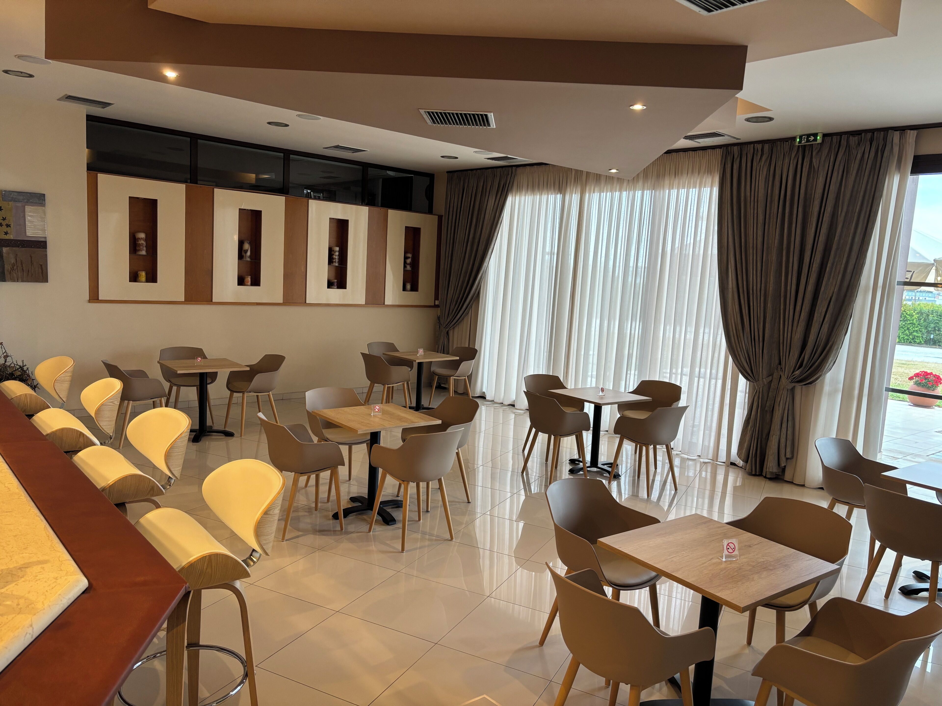 Un café moderno con diversas opciones de asientos, incluyendo mesas y sillas, y una zona de bar con taburetes.