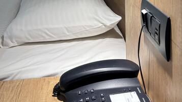 A hotel room with a wooden headboard, a bed with white linens, a black telephone, and a wall-mounted power outlet.