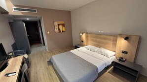 A modern hotel room with a bed, bedside table, desk, chair, and a painting on the wall. - Achillio Hotel (Komotini)