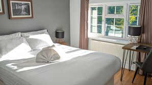 Un dormitorio con cama, mesita de noche, lámpara, silla y ventana con cortinas.