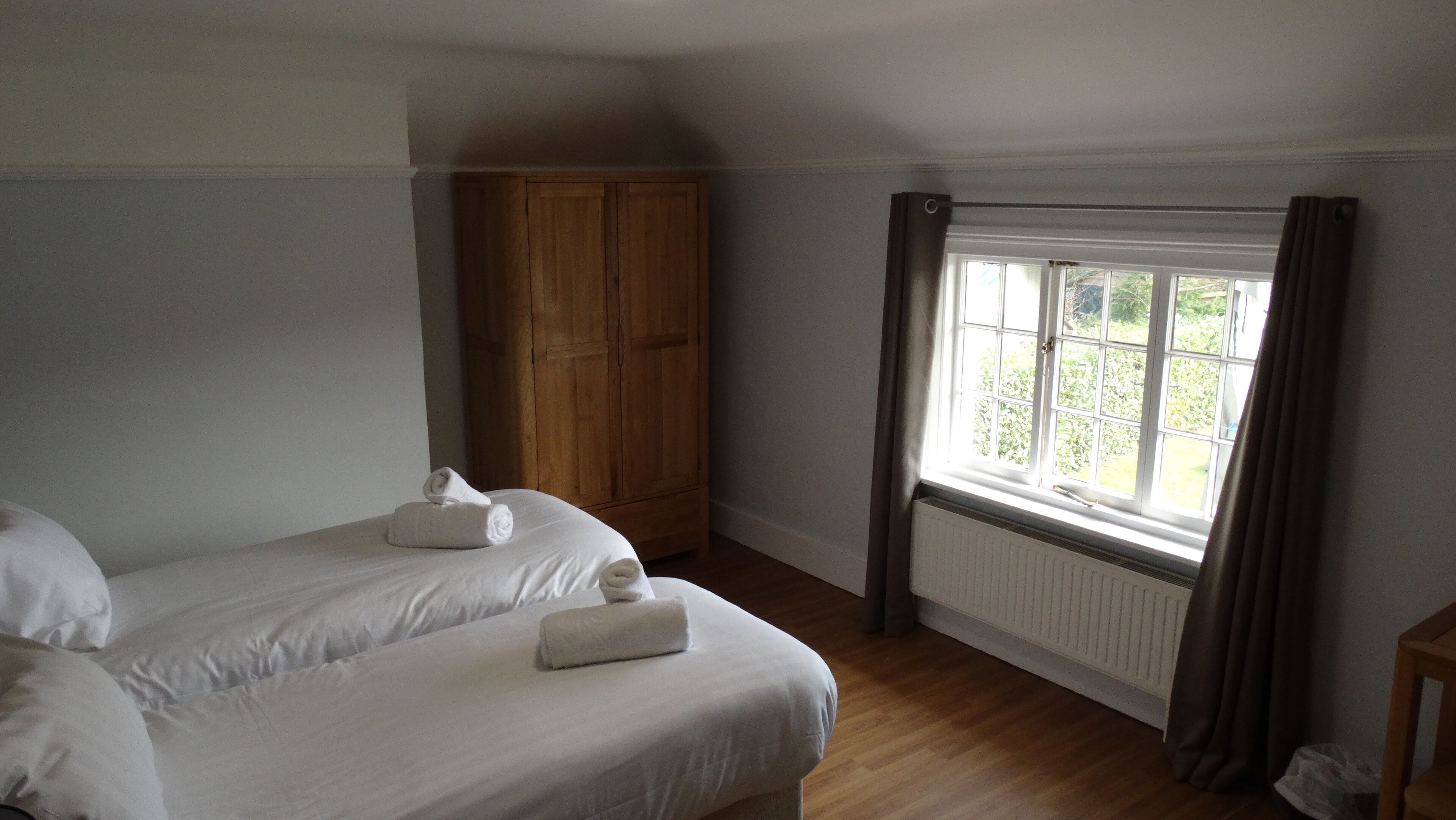 Ein Schlafzimmer mit zwei Betten, einem Holzschrank, einem Fenster mit Vorhängen und einer Heizung.