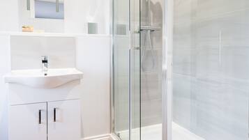 Un baño moderno con ducha acristalada, lavamanos blanco y suelo de madera.