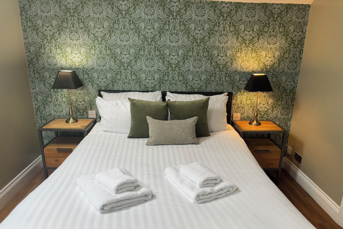 Una cama bien hecha con almohadas, dos lámparas de noche y una pared con estampado floral.