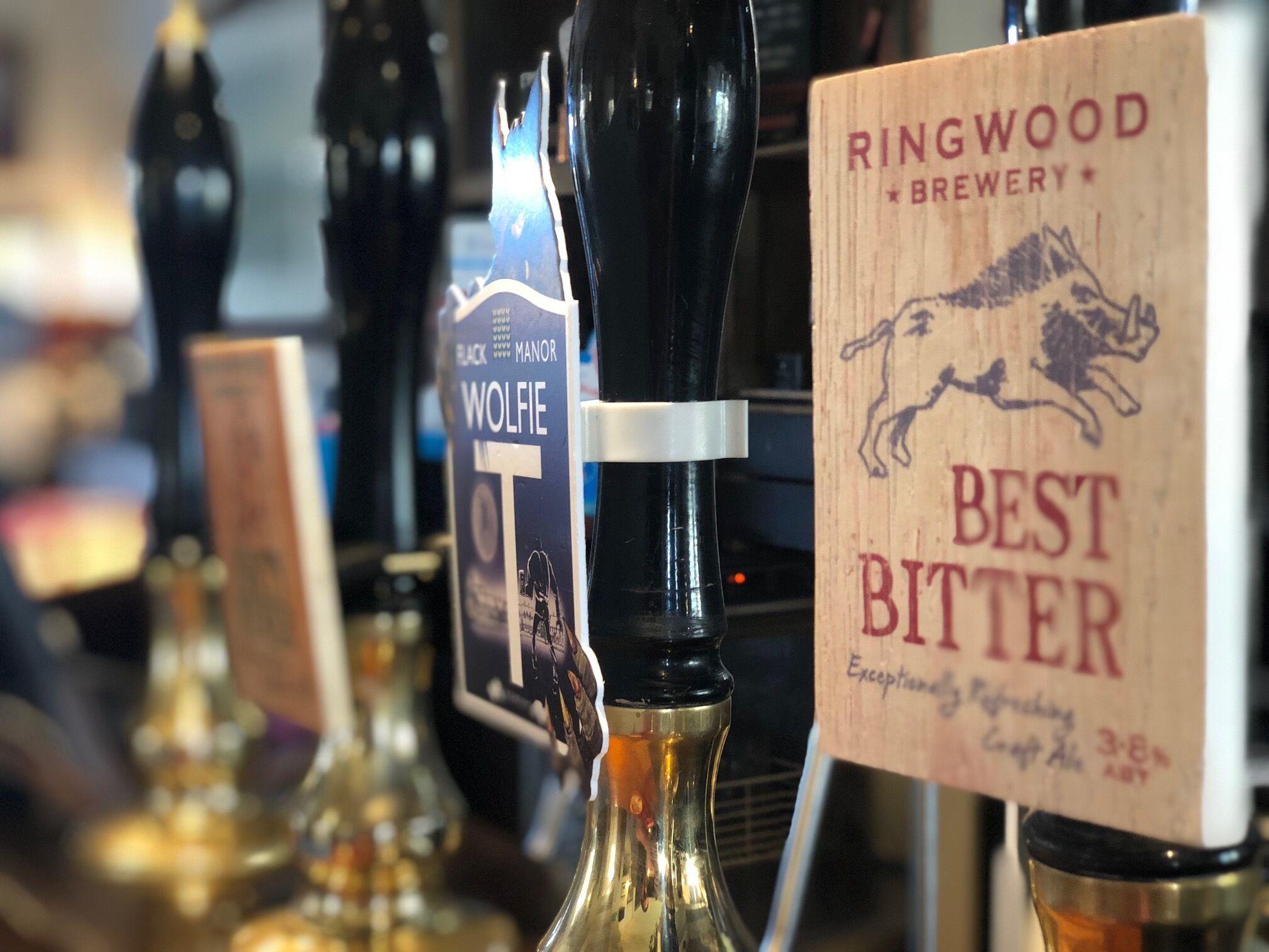 Variedad de grifos de cerveza con etiquetas que indican diferentes marcas y tipos, incluyendo 'Wolfie' y 'Ringwood Brewery Best Bitter'.
