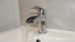 A modern bathroom sink with a chrome faucet and clear running water. - The Mortimer Arms  (Romsey)