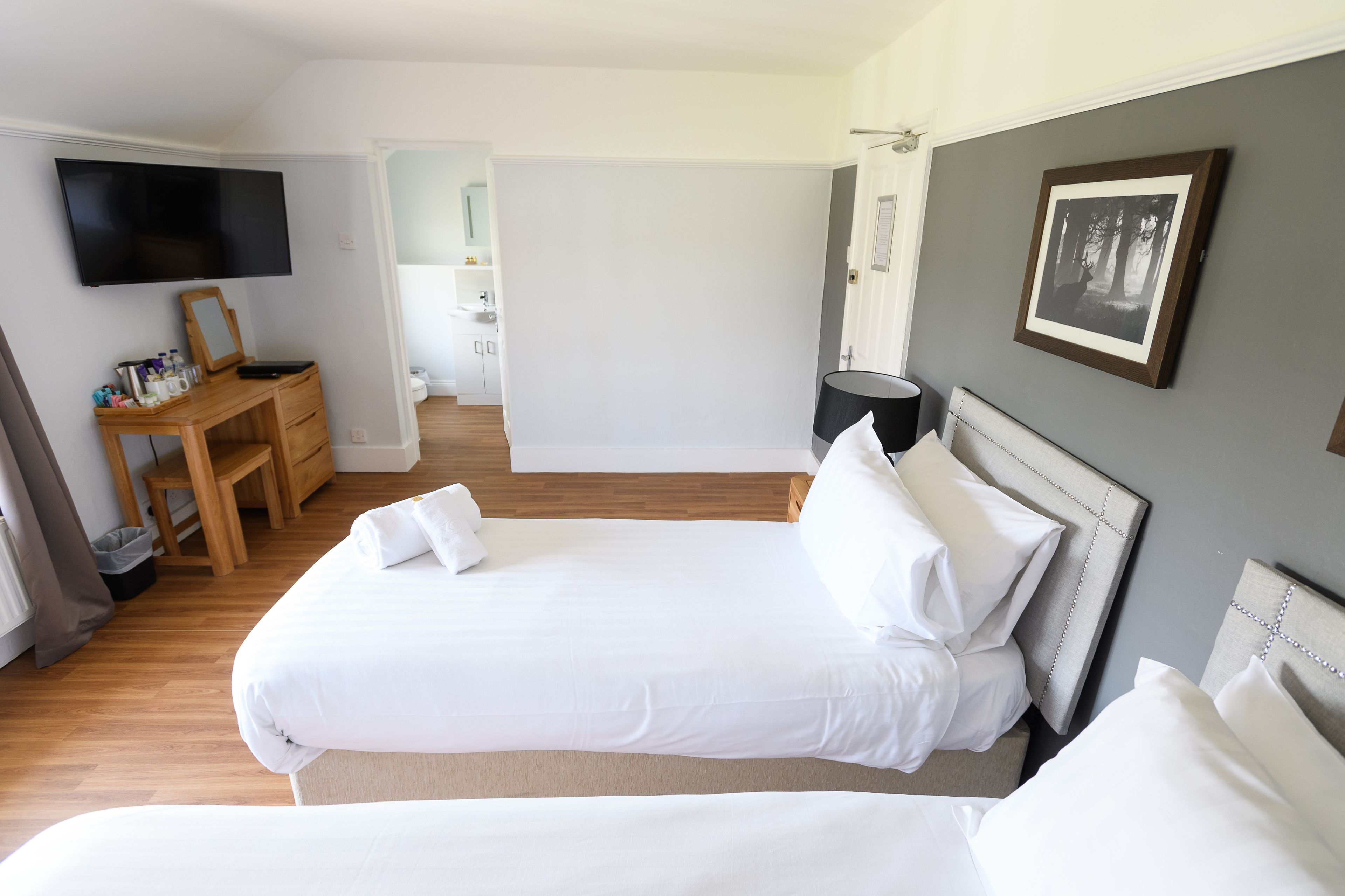 Un dormitorio con cama, escritorio, silla, televisor y un cuadro en la pared.