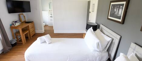 A bedroom with a bed, a desk, a chair, a TV, and a framed picture on the wall.