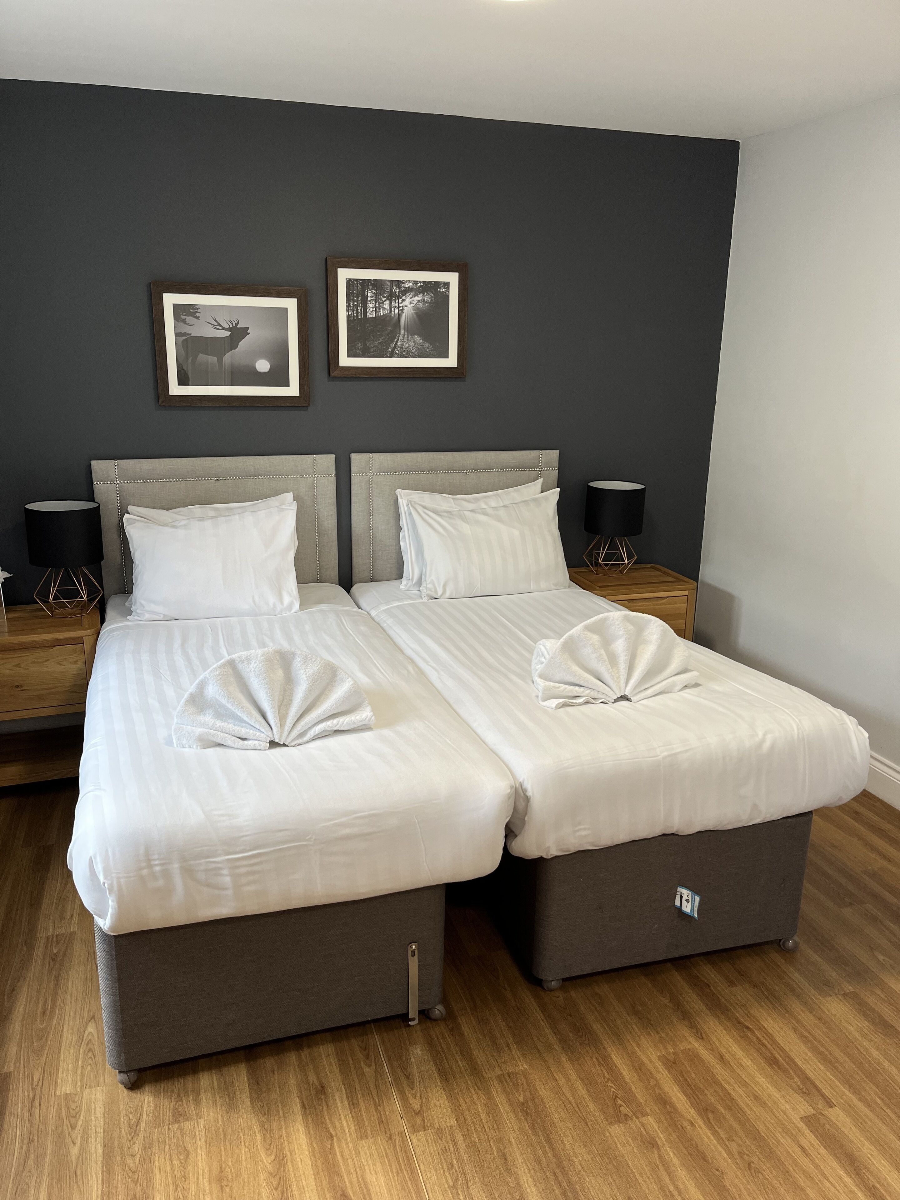 Una cama doble con dos mesitas de noche, una pared oscura y dos cuadros enmarcados.