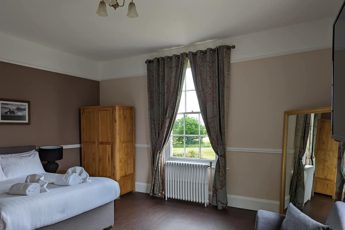 Quarto de hotel com uma cama, um guarda-roupa de madeira, um radiador e uma janela com cortinas.