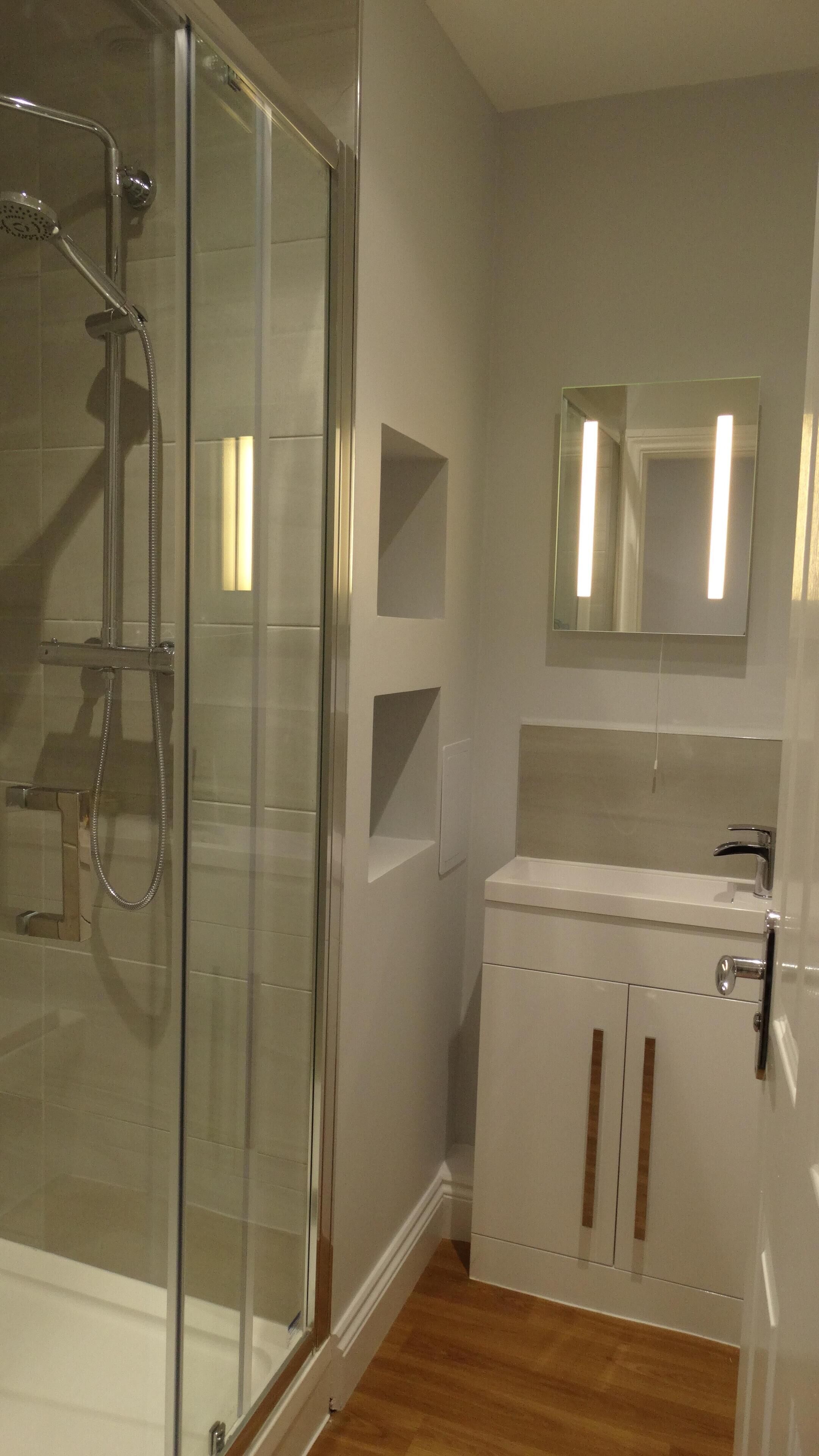Un baño con cabina de ducha de vidrio, un lavamanos blanco y un espejo sobre él.