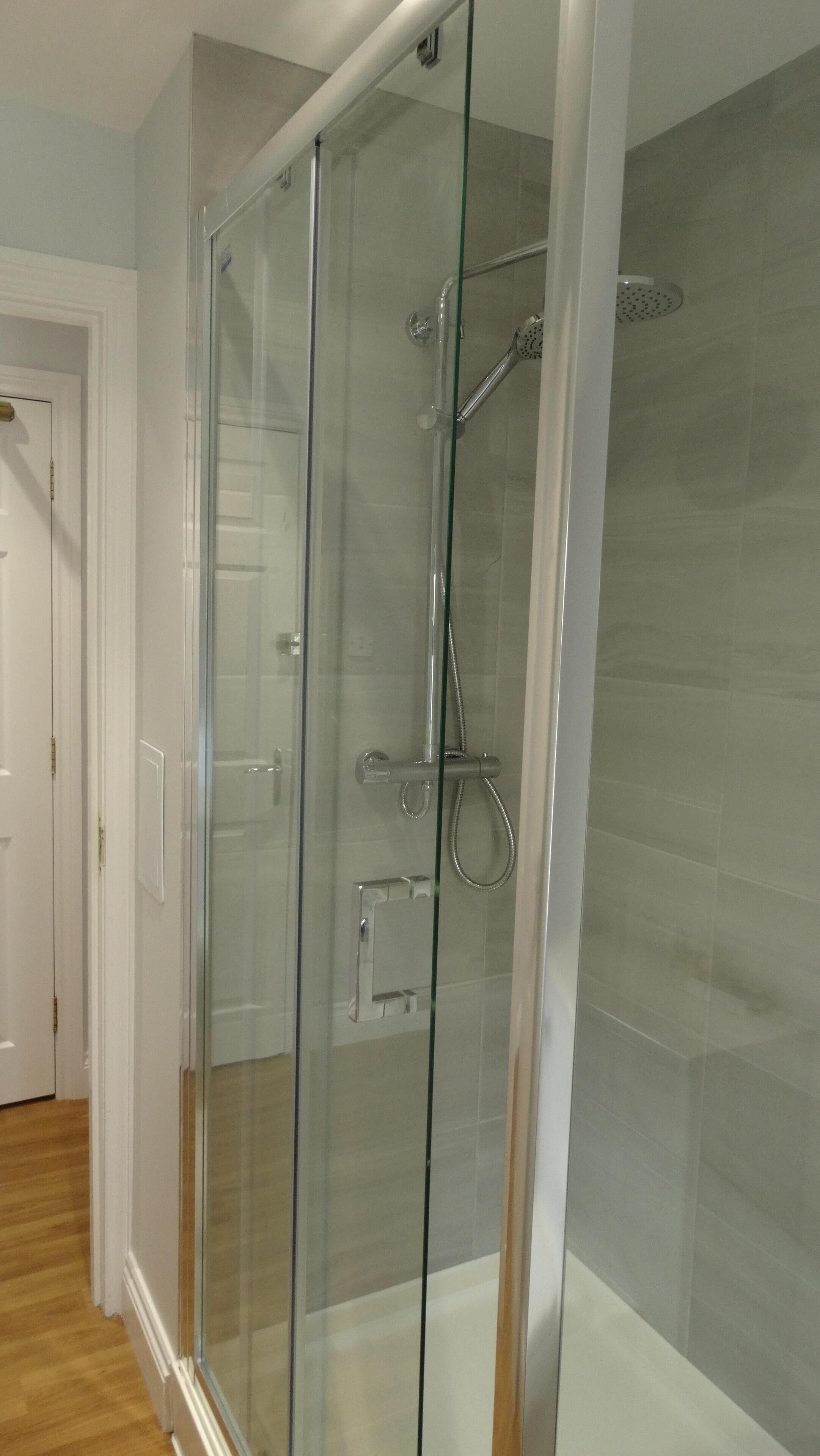 A glass-enclosed shower stall with a handheld showerhead and a handheld shower head.