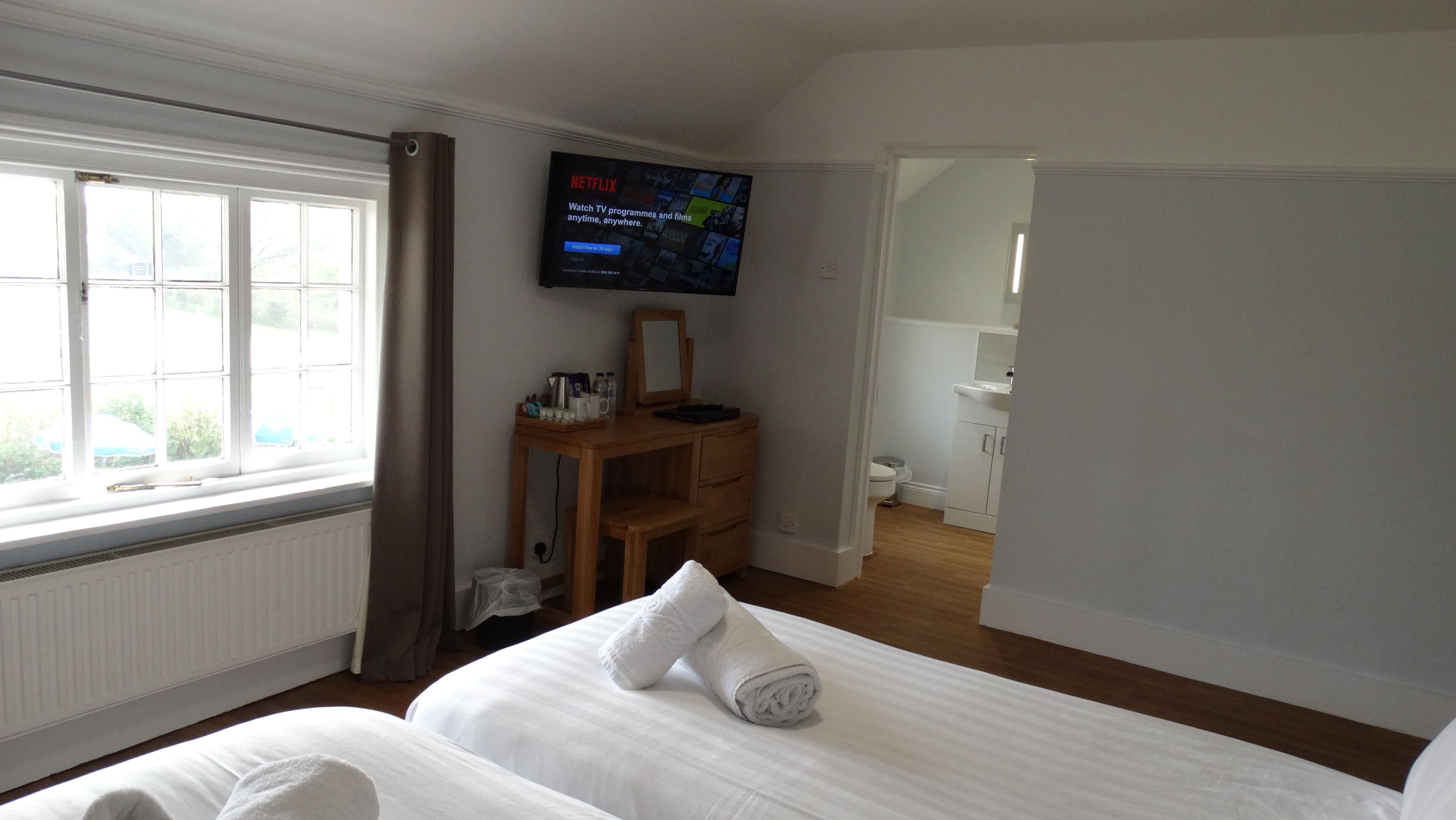 Una habitación de hotel con cama, escritorio, televisor, ventana y baño.