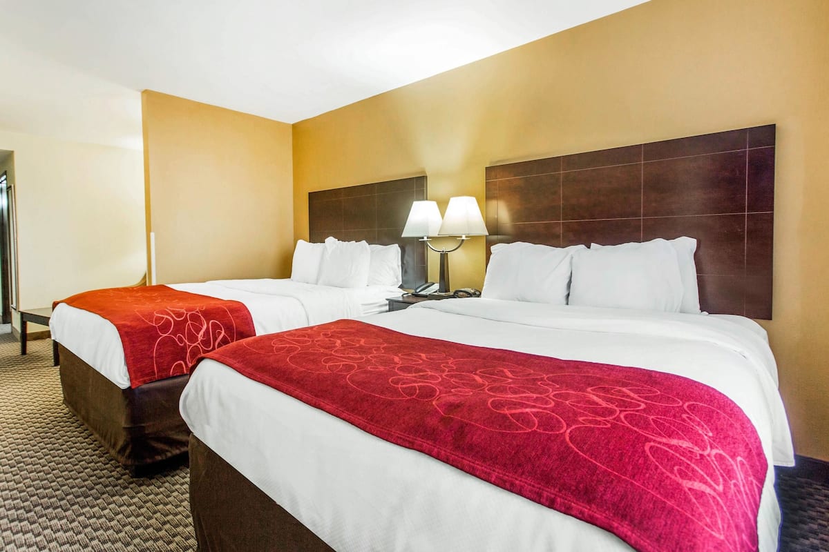A hotel room with two beds, each with a red and white blanket, a nightstand with a lamp, and a headboard with a grid pattern.