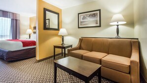 Habitación de hotel con cama, sofá, mesa de centro, dos lámparas, un cuadro enmarcado y un espejo.