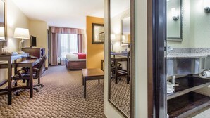 Una habitación de hotel con escritorio, silla, cama y baño con lavabo y espejo.