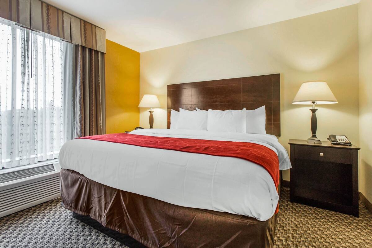 A hotel room with a large bed, two bedside lamps, a nightstand with a phone, and a window with curtains.