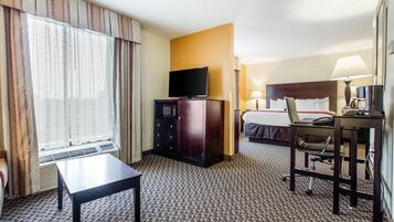 Habitación de hotel con cama, escritorio y silla, televisor, lámpara de escritorio y ventana con cortinas.