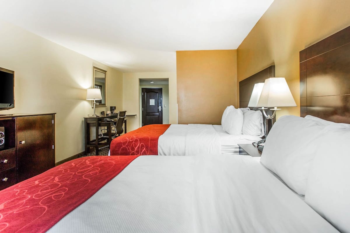 A hotel room with two beds, a desk, a TV, and a door leading to a hallway.