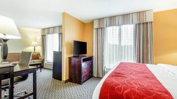 Una habitación de hotel con una cama, un escritorio con silla, un televisor en una cómoda y una ventana con cortinas.