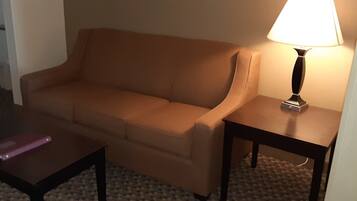 A beige sofa, a small table with a lamp, and a pink book on a carpeted floor.