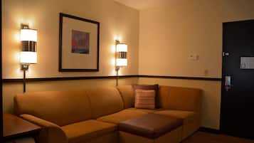A hotel room with a sectional sofa, two wall-mounted lamps, a framed picture, and a door with a lock.