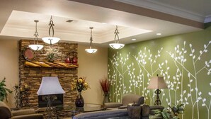 A modern living room with a stone fireplace, green wall with white branches, a sofa, a coffee table, and two lamps.
