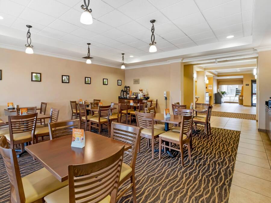 Uma sala de jantar de hotel com várias mesas e cadeiras de madeira, um tapete estampado e luminárias no teto.