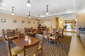 A hotel dining area with multiple wooden tables and chairs, a patterned carpet, and ceiling lights.