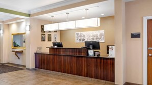 A reception area with a wooden reception desk, two computer monitors, framed certificates, and a wall-mounted artwork.