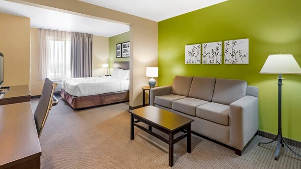 A hotel room with a bed, a sofa, a coffee table, a desk, and a lamp.