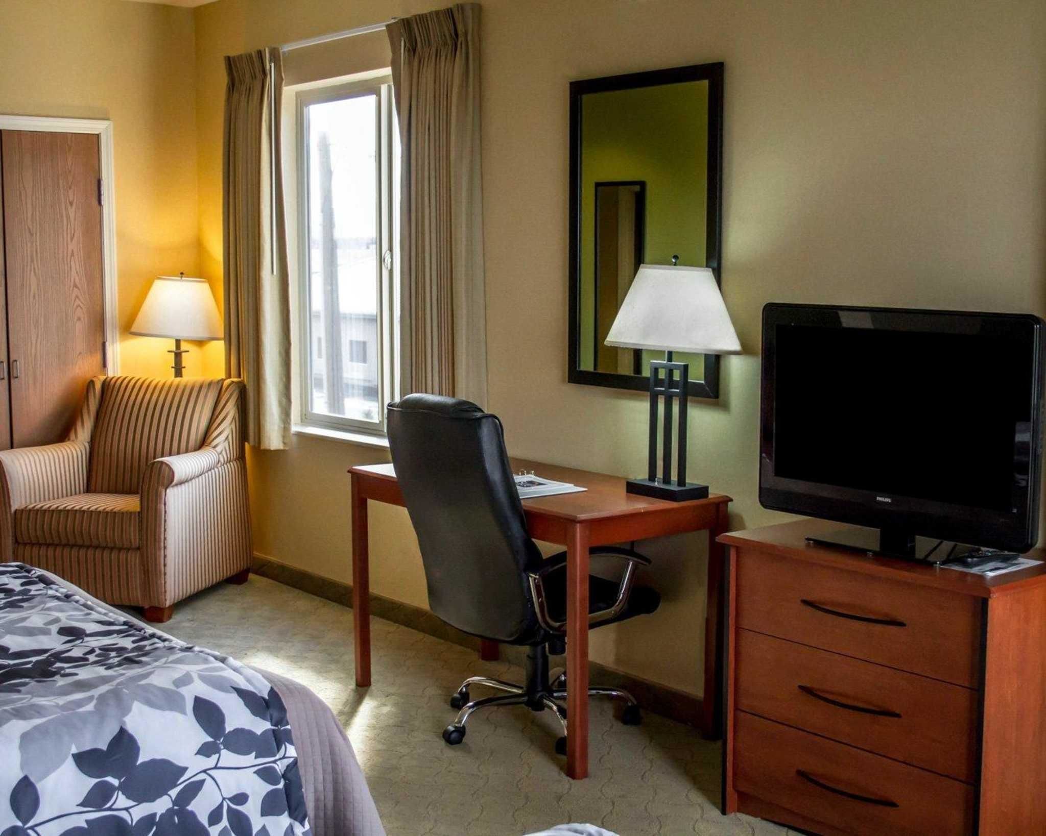 Ein Hotelzimmer mit Bett, Schreibtisch, Stuhl, Fernseher, Lampe und Spiegel.